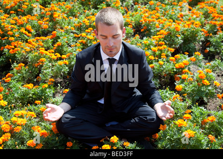 Businessman meditating among flowers Stock Photo