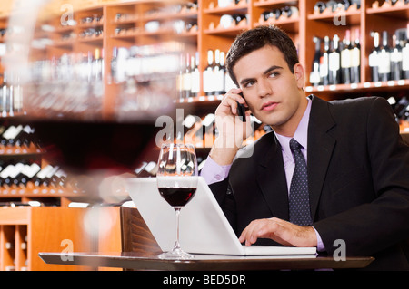 Businessman talking on a mobile phone and using a laptop in a bar Stock Photo