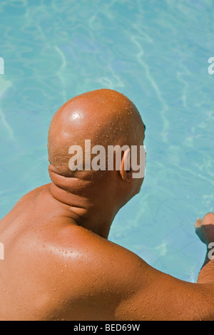 Bald senior citizen sitting at the edge of a swimming-pool Stock Photo