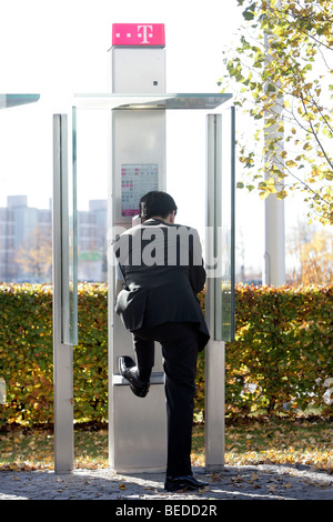 Businessman making a phone call in a public Telekom telephone box, Munich, Bavaria, Germany, Europe Stock Photo