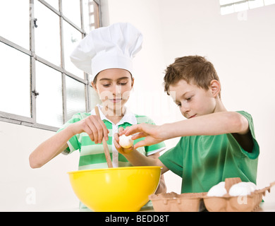 Girl wearing a chef's hat and a boy cracking eggs into a bowl Stock Photo