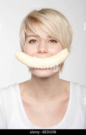 Young woman with short blonde hair, banana in her mouth Stock Photo