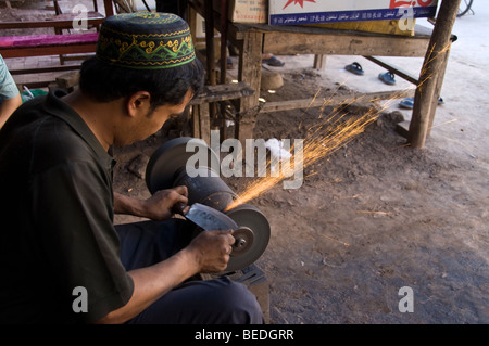 Local Uighur sharpening a knife in a street market of Kashgar, Xinjiang Province, China. Stock Photo