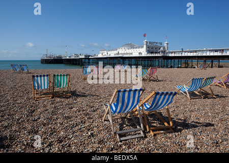 Deck chairs on pebble beach with Brighton Pier behind. Stock Photo