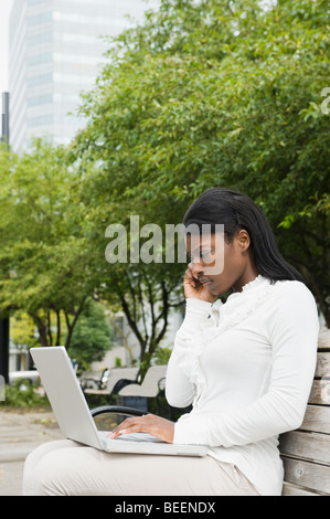 African businesswoman using laptop on bench in city Stock Photo
