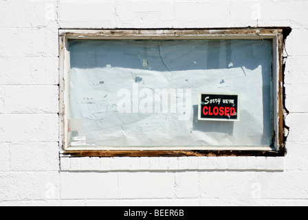 boarded up white window of bankrupt business with 'Sorry we're closed' sign Stock Photo