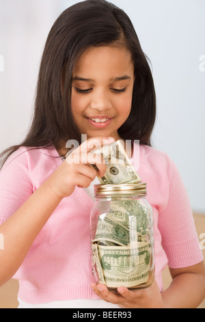 Hispanic girl putting money in jar Stock Photo