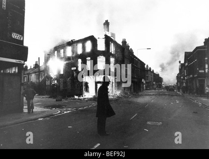 Flames pour from a gutted building in Toxteth, near Liverpool with a lone policeman standing guard after a long night of rioting Stock Photo