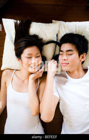 Asian Young couple lying on floor wearing headphones, eyes closed Stock Photo