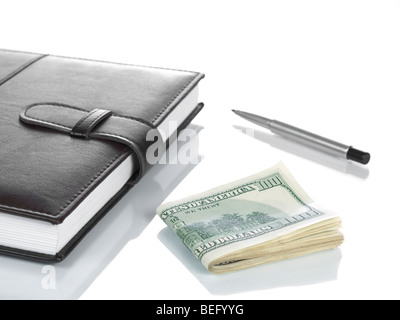 An agenda with several hundred dollar bills and a pen, isolated on white. Stock Photo