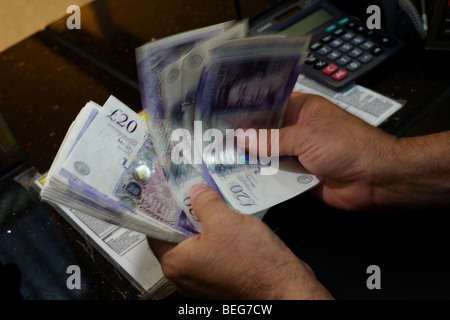 An assistant counts through blurred Pounds Sterling notes at the Travelex bureau de change at Heathrow Airport's Terminal 5. Stock Photo