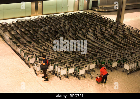 Airline passengers collect trolleys in the baggage reclaim hall in the arrivals of Heathrow Airport's Terminal 5. Stock Photo