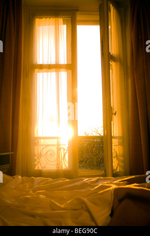 sunrise coming through the shutters of a parisain hotel room, illuminating the unmade bed Stock Photo