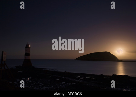 Penmon Lighthouse at dusk with full moon rising by Puffin Island at low tide. Penmon Point Anglesey North Wales UK Stock Photo