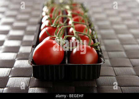 Red tomatoes branch un a black plastic box over brown tablecloth Stock Photo
