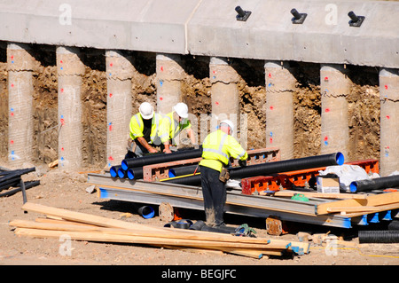 Workmen beside exposed concrete piles which form part of a retaining wall structure for a motorway bridge Stock Photo