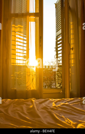 sunrise coming through the shutters of a parisain hotel room, illuminating the unmade bed Stock Photo