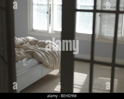 Unmade bed with ruffled blanket in a bedroom Stock Photo