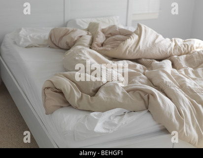 Unmade bed with ruffled blanket Stock Photo
