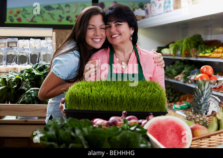 Portrait of a mature woman and her daughter standing with a tray of wheatgrass in a grocery store and smiling Stock Photo