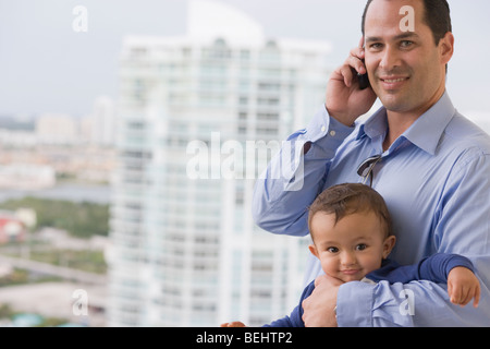 Man talking on a mobile phone and holding his son Stock Photo