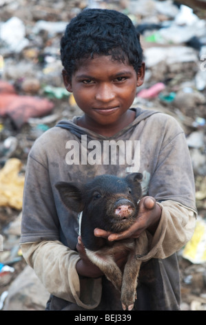 Lower caste Indian boy with small pig in a rubbish tip. Andhra Pradesh, India Stock Photo