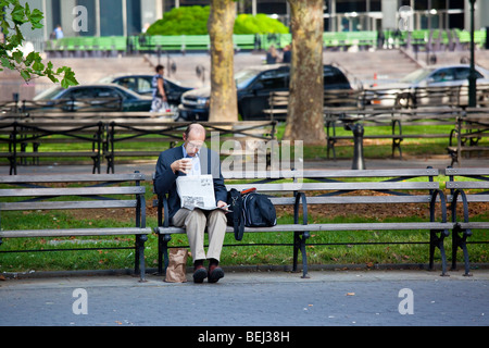 Man reading newspaper and drinking coffee on a park bench in downtown Manhattan New York City Stock Photo