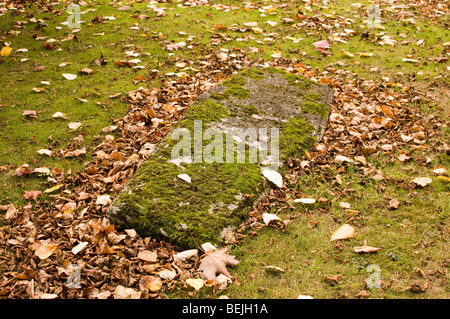 A long-forgotten grave covered in autumn leaves, and moss, in a graveyard. Stock Photo