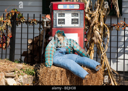 A headless scarecrow sitting on a bale of hay in front of a vintage Mobil gas pump. Stalks of corn and Halloween ivy. Stock Photo