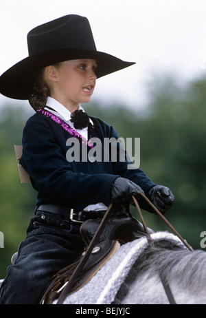 Child wearing cowboy hat sitting on horse holding reins riding in horse show Stock Photo