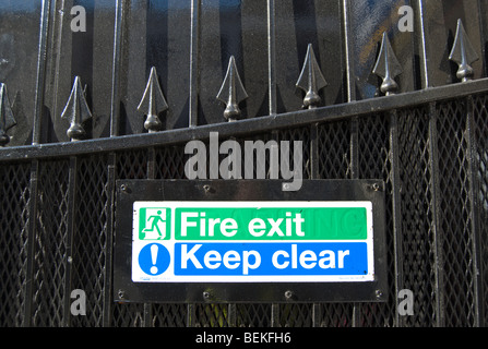 fire exit sign and keep clear sign fixed to a cast iron gate with arrowhead decoration, in queensway, london, england Stock Photo