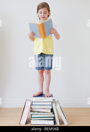 Child reading while standing on books Stock Photo