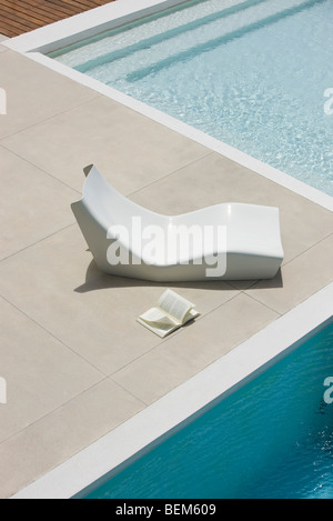 Open book lying on ground next to poolside deckchair, high angle view Stock Photo