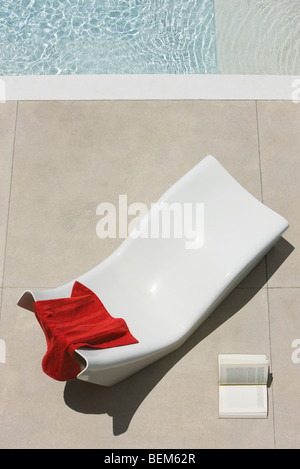 Towel left on poolside deckchair, open book lying on ground nearby Stock Photo