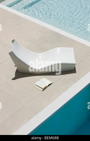 Open book lying on ground next to poolside deckchair Stock Photo