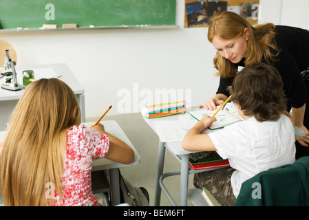 Elementary teacher leaning over student's desk, helping him with assignment Stock Photo
