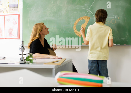 Boy standing in front of classroom blackboard, using protractor Stock Photo