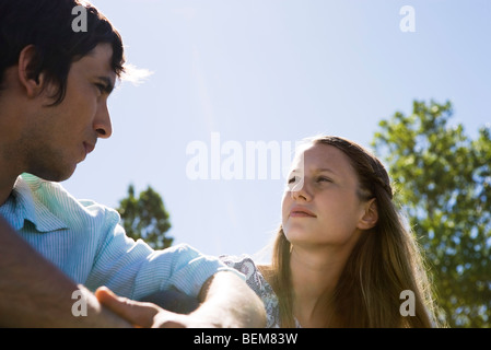 Young couple sitting outdoors, looking at each other Stock Photo