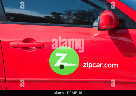 A close up of a Zipcar logo on a red car. Zip Car is a carsharing company whose customers pay by the hour or day. Stock Photo