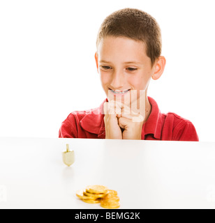 Boy watching a Hanukkah dreidel spin, with chocolate gelt in the foreground. Isolated on white. Stock Photo