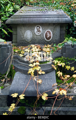 Old pictures on forgotten overgrown family grave / tomb covered in vegetation at cemetery in autumn Stock Photo