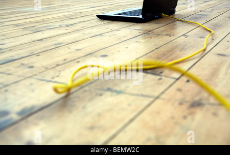 Laptop on wooden floor with yellow ethernet cable Stock Photo