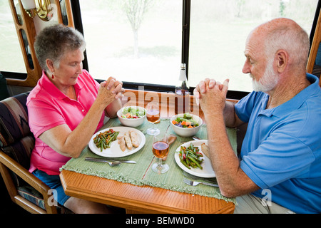 Senior couple say grace before eating a meal in their motor home. Stock Photo