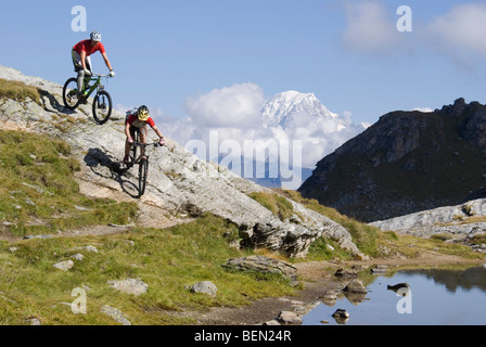 Two mountain bikers ride down a rocky slope next to a lake in the mountains near Les Arcs in the French Alps. Stock Photo