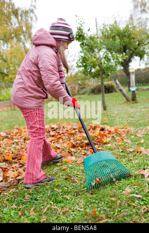 Little girl rake colorful fallen autumn leaves in garden Stock Photo