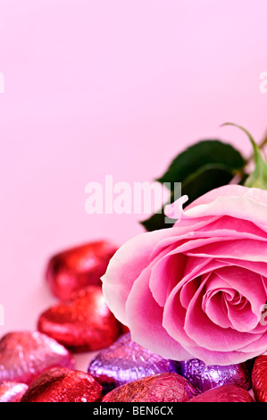 Pink rose with Valentine's chocolates wrapped in red and purple foil Stock Photo