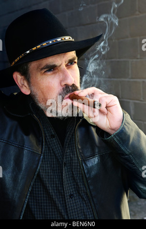 Man with beard in cowboy hat smoking cigar Stock Photo