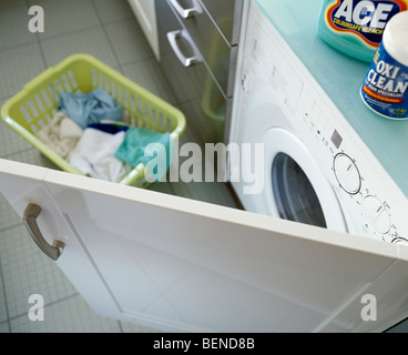Close-up of plastic basket of laundry on floor below washing machine behind open cupboard door Stock Photo