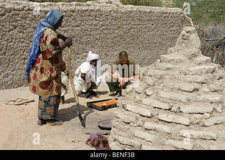 Tourist looking at native black people baking bread in stone oven of bakery, Chad, Central Africa Stock Photo