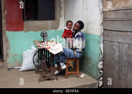 Seamstress with child working with old Usha treadle sewing machine at home, Ruhengeri, Musanze, Rwanda, Central Africa Stock Photo